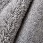 Close-up of grey marl brushed fleece across a soft fold, showing the dense brushed pile and the heathered fibre mix on one side and the smooth matte knit face on the other