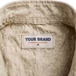 Close-up of the inside back neck of the stone cotton canvas fishing vest showing the cream woven YOUR BRAND label with navy lettering, a red rule line and the size M mark, stitched in below the collar band
