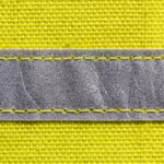 Close-up of the fluorescent yellow woven polyester shell of the high visibility jacket with a silver-grey reflective tape band stitched along both edges, showing the yarn weave and the beaded tape face
