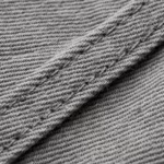 Close-up of the stone grey cotton poly-cotton twill weave of the men's industrial coverall, showing the diagonal ribs, yarn structure, cotton fibres and a felled seam