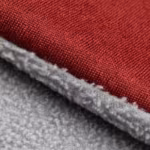 Close-up of the red softshell cloth folded at the edge, showing the fine woven face bonded to the grey brushed fleece backing