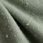 Close-up of the sage green cotton single jersey of the pyjama set showing the fine knit stitch columns, twisted yarns and natural fibre fly across a soft fold