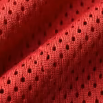 Close-up of the red polyester eyelet mesh of the sports jerseys, showing the perforated mesh holes, knit loops and yarn fibres across a soft fold