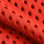 Close-up of the red polyester eyelet mesh of the team wear range, showing the perforated mesh holes, knit loops and yarn fibres across a soft fold