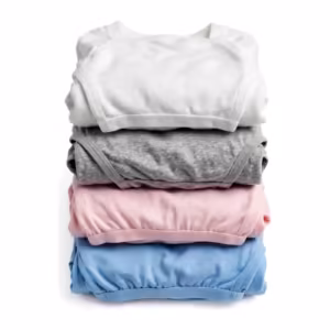 Folded stack of knit undergarments in white, grey marl, soft pink and sky blue - a folded cotton rib vest over folded briefs and a trunk, showing the matte jersey and rib knit of the whole program