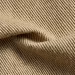 Close-up of the khaki cotton twill weave of the work clothes, showing the diagonal ribs, yarn structure and fibre hairs across a soft fold